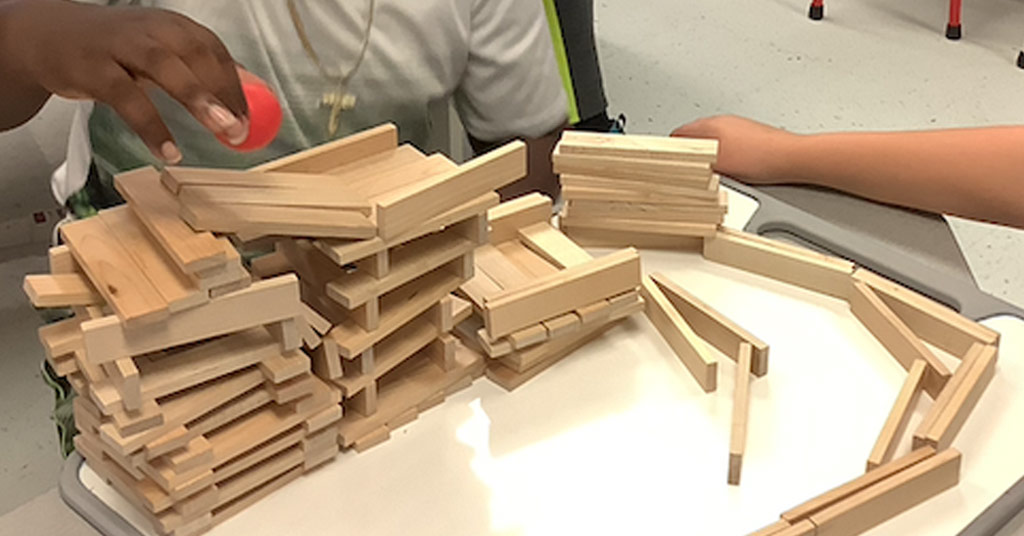Student building a Keva Block Challenge structure on a whiteboard using wooden planks and a ping pong ball