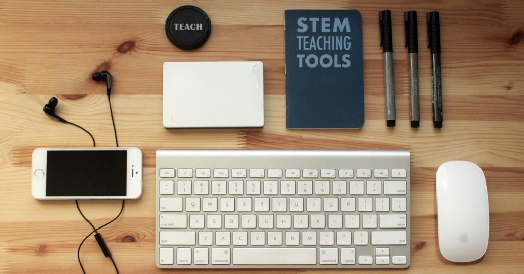 Desk with STEM teaching tools including a keyboard, notebook, smartphone, earbuds, mouse, and markers.